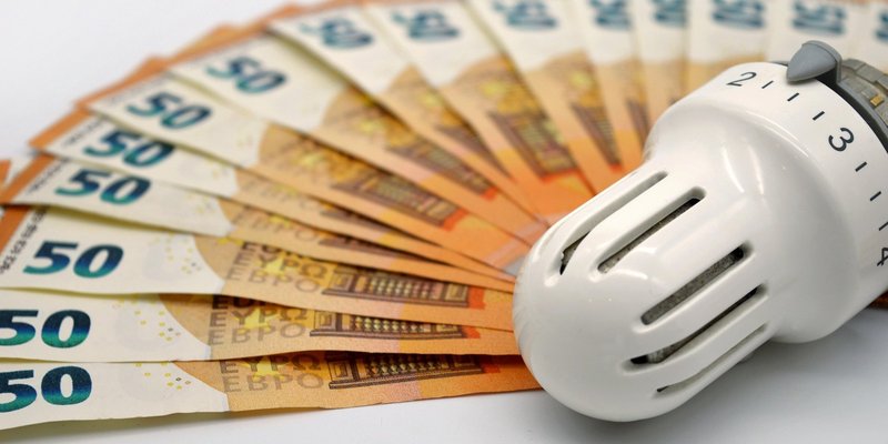 Ein Thermostat liegt neben einem Fächer von Geldscheinen.